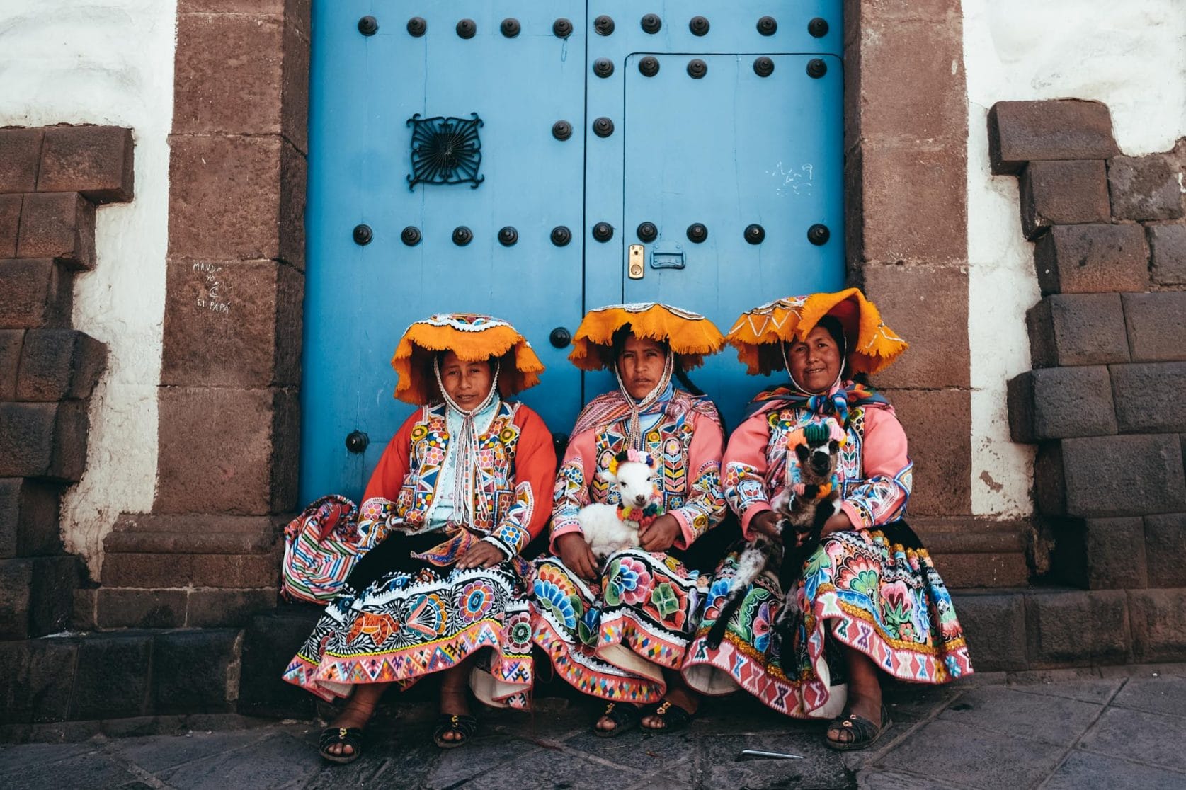 Cusco women in their traditional clothing sitting beneath a blue door