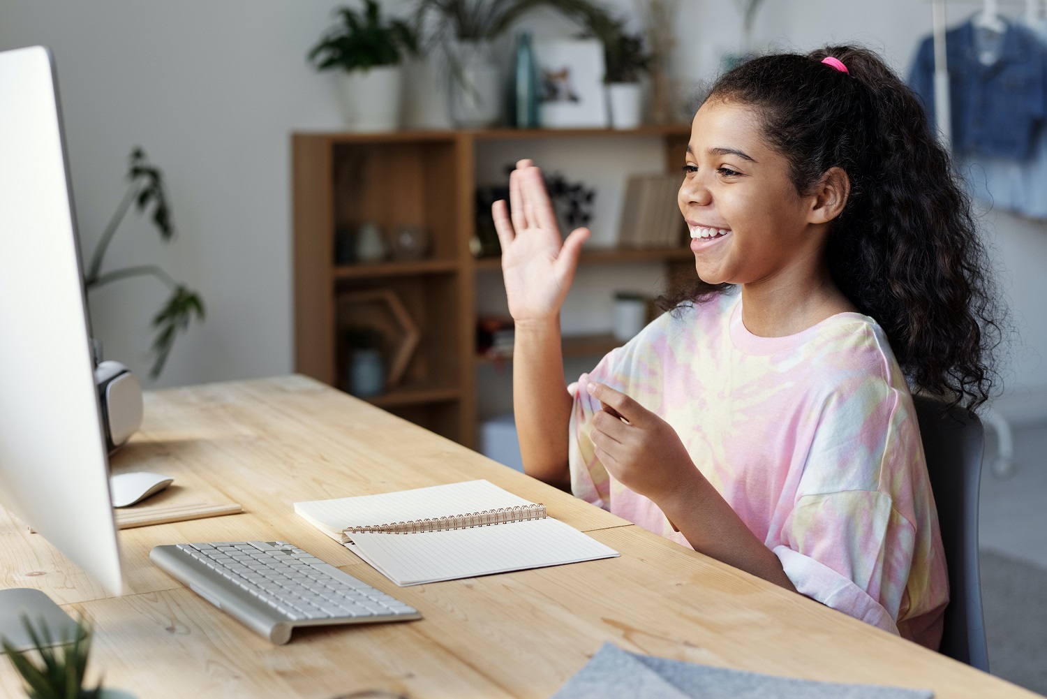 child in pink, sittin in front of a computer raising her hand