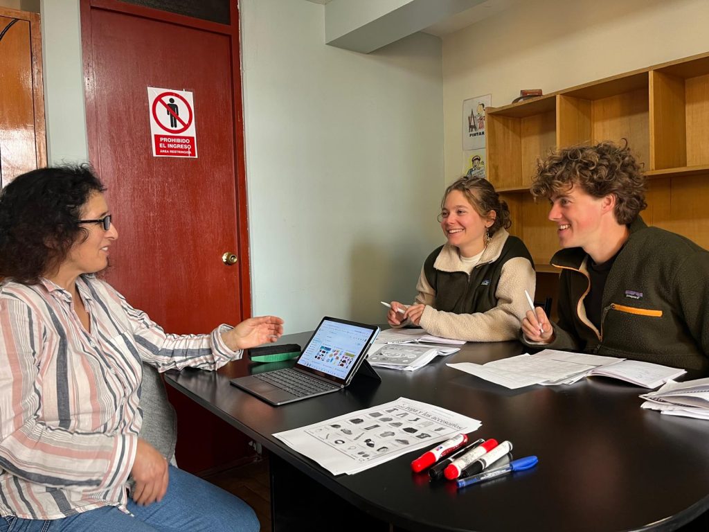 Local Cusqueña Spanish teacher conducting a Spanish lesson with two European students in a naturally lighted room with Ipad and homework sheets on black desk. 