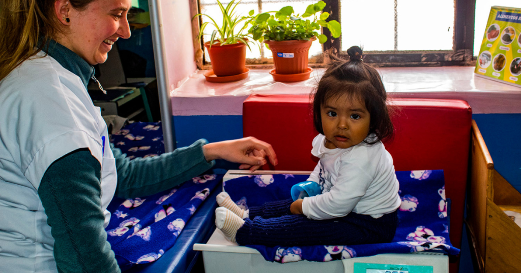 Medical volunteers uses Spanish phrases to explain the process while weighing a child in Cusco