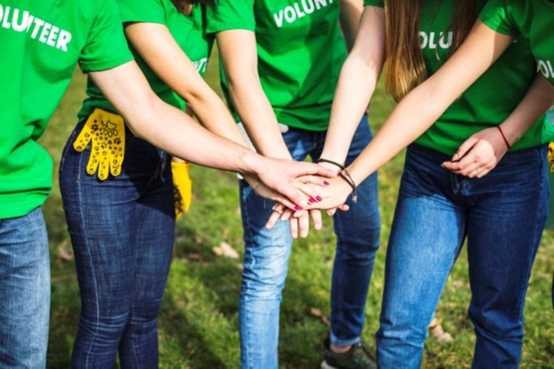 A group wearing green VOLUNTEER shirts stands in a circle, hands joined, symbolizing teamwork and unity during their volunteering journey in Cusco Peru.