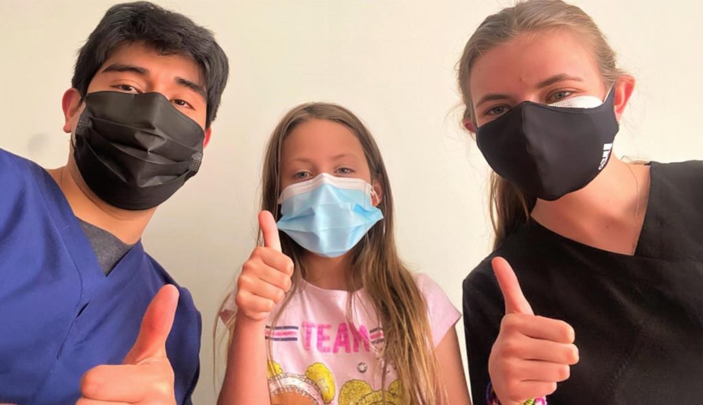 A doctor, volunteer and young girl make a thumbs up to the camera